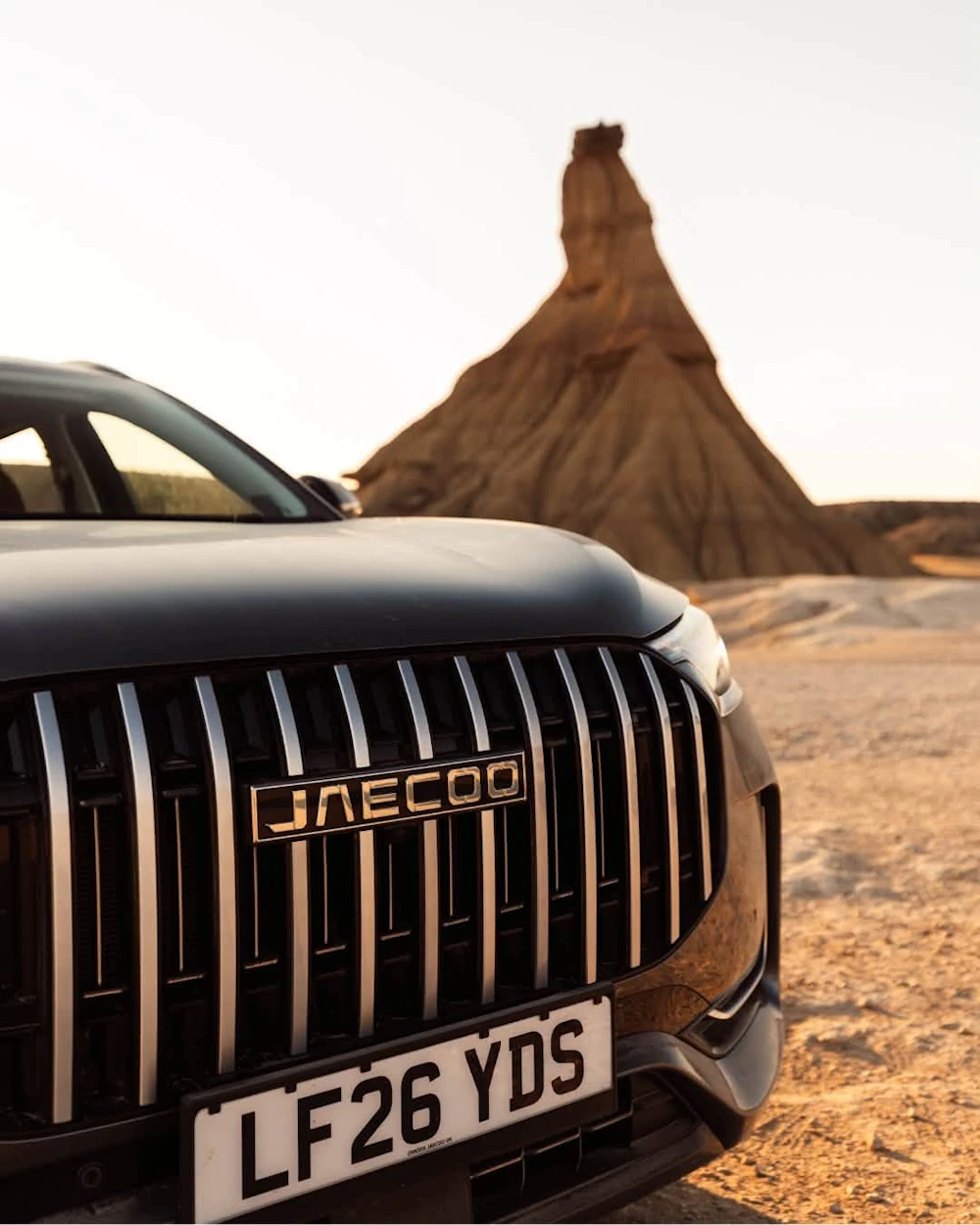 Close-up of the JAECOO 8 grille with a Spanish rock formation behind it