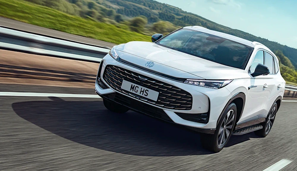 White MG HS Plug-in Hybrid driving on a road beside green hills
