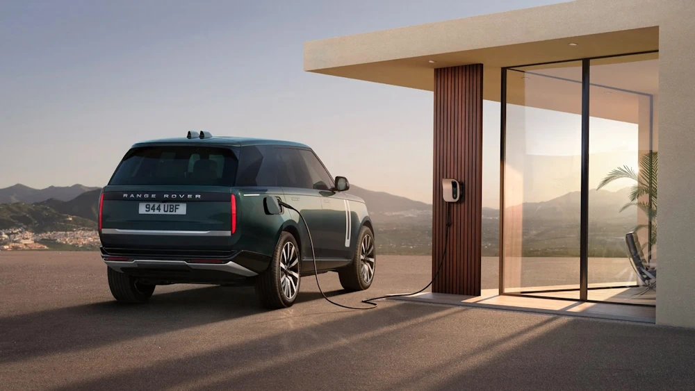 Range Rover Electric connected to a charger beside a house
